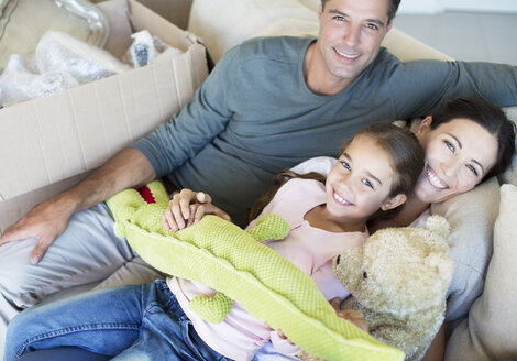 Porträt einer lächelnden Familie mit Plüschtieren auf dem Sofa - CAIF18572