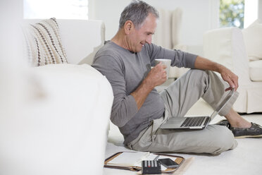 Senior man using laptop on living room floor - CAIF18603