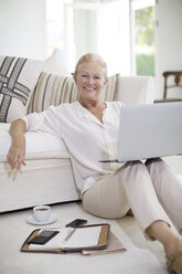 Ältere Frau benutzt Laptop auf dem Boden ihres Wohnzimmers - CAIF18611