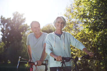 Senior couple walking bicycles in park - CAIF18612