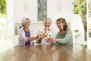 Senior women toasting wine glasses in kitchen - CAIF18614