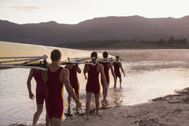 Rowing team carrying scull into lake at dawn - CAIF18629