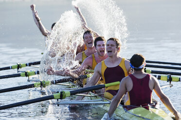 Rowing team splashing and celebrating in scull on lake - CAIF18631