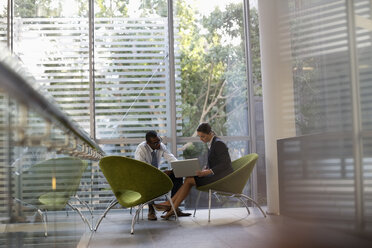 Businessman and businesswoman using laptop in lobby - CAIF18640