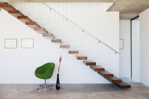 Stuhl unter schwebender Treppe in modernem Haus - CAIF18787