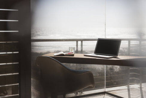 Laptop auf dem Schreibtisch im modernen Heimbüro mit Blick aufs Meer - CAIF18795