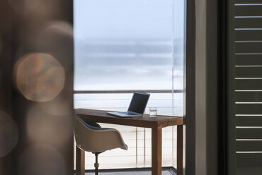 Laptop auf dem Schreibtisch im modernen Heimbüro mit Blick aufs Meer - CAIF18797