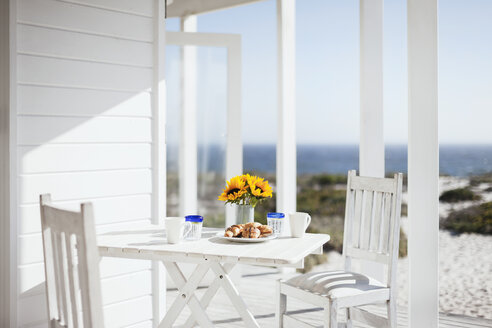 Blumenvase, Kaffee und Gebäck auf dem Terrassentisch mit Blick aufs Meer - CAIF18878