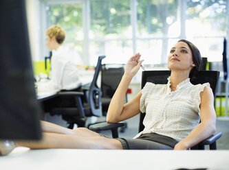 Geschäftsfrau entspannt sich mit hochgelegten Füßen auf dem Schreibtisch im Büro - CAIF18891