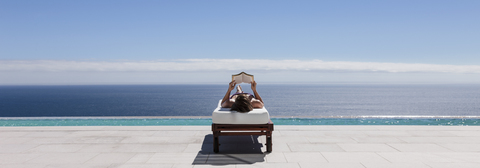 Frau entspannt sich auf einem Liegestuhl am Pool mit Blick auf das Meer, lizenzfreies Stockfoto