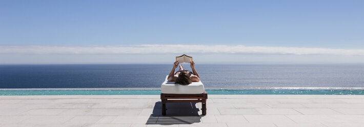 Frau entspannt sich auf einem Liegestuhl am Pool mit Blick auf das Meer - CAIF18979