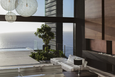 Sofas and tables in modern living room overlooking ocean - CAIF19016