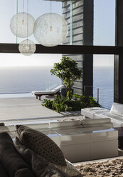 Sofas and tables in modern living room overlooking ocean - CAIF19018