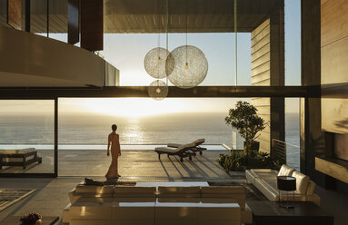 Woman in modern house overlooking ocean - CAIF19023