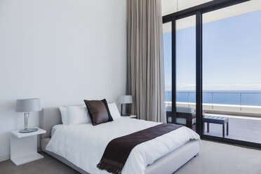 Bed and lamps in modern bedroom overlooking ocean - CAIF19036
