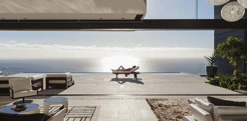 Frau beim Sonnenbaden auf einem Liegestuhl am Pool mit Blick auf das Meer - CAIF19040