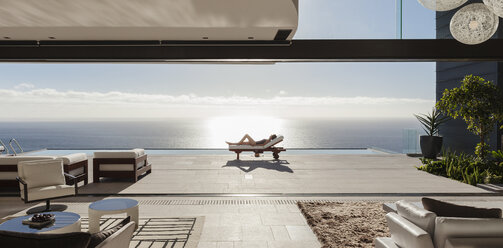 Woman sunbathing on lounge chair at poolside overlooking ocean - CAIF19040