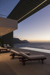 Balcony of modern house overlooking ocean at sunset - CAIF19047