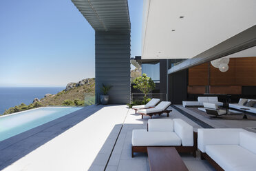Lounge chairs and infinity pool on modern patio overlooking ocean - CAIF19049