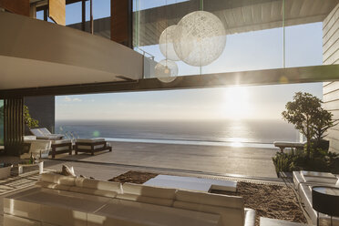 Modern living room overlooking ocean at sunset - CAIF19051