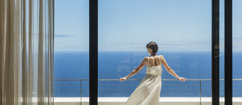 Frau schaut vom Balkon aufs Meer, lizenzfreies Stockfoto