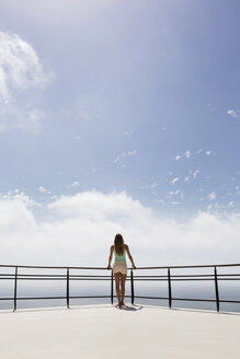 Frau steht auf einem Balkon mit Blick auf das Meer - CAIF19109