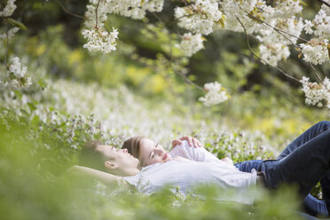 Couple laying in grass under tree with white blossoms - CAIF19198