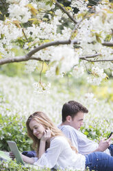 Couple using digital tablet and cell phone in park - CAIF19203