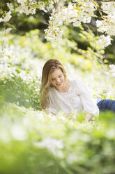 Frau liest Buch im Gras unter einem Baum mit weißen Blüten - CAIF19205