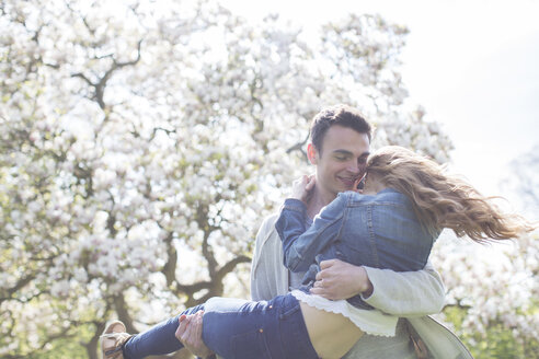 Mann hebt Frau unter Baum mit weißen Blüten - CAIF19212