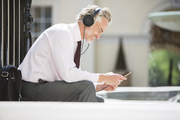 Businessman listening to headphones on city street - CAIF19217
