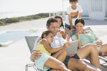 Familie benutzt digitales Tablet im Liegestuhl am Pool - CAIF19279