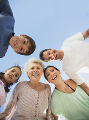 Multi-generation family smiling in huddle against blue sky - CAIF19280