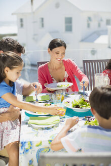 Familie beim Mittagessen am Tisch auf der sonnigen Terrasse - CAIF19284