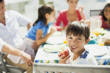 Boy eating fruit with family at table on sunny patio - CAIF19286