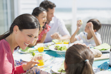 Familie beim Mittagessen am Tisch auf der sonnigen Terrasse - CAIF19287