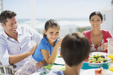 Familie beim Mittagessen am Tisch auf der sonnigen Terrasse - CAIF19290