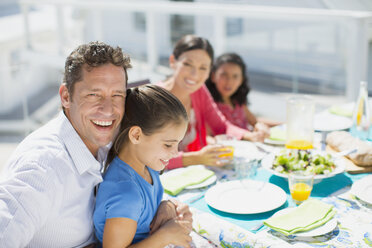 Familie beim Mittagessen am Tisch auf der sonnigen Terrasse - CAIF19291