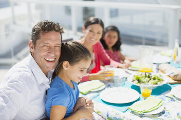 Family eating lunch at table on sunny patio - CAIF19291