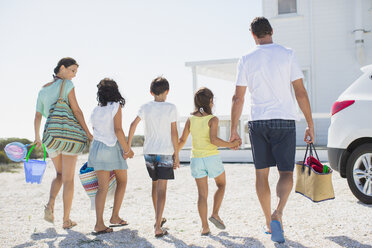 Familie hält sich an den Händen und trägt Strandausrüstung in der sonnigen Einfahrt - CAIF19300