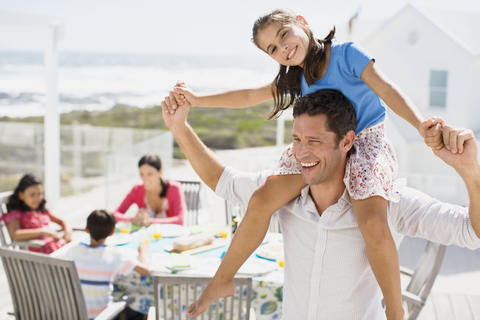 Father carrying daughter on shoulders on sunny patio stock photo