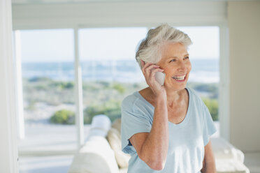 Ältere Frau, die im sonnigen Wohnzimmer mit ihrem Handy telefoniert - CAIF19308