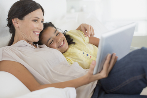 Mutter und Tochter benutzen ein digitales Tablet auf dem Sofa, lizenzfreies Stockfoto