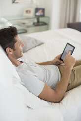 Mann mit digitalem Tablet auf dem Bett - CAIF19365