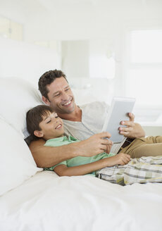 Vater und Sohn benutzen ein digitales Tablet auf dem Bett - CAIF19375