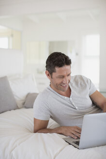 Mann mit Laptop auf dem Bett - CAIF19379