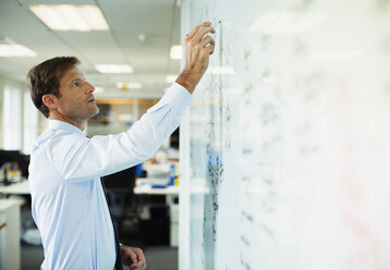 Businessman writing on whiteboard in office - CAIF19398