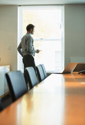 Businessman standing at conference room window - CAIF19406