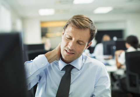 Geschäftsmann reibt sich im Büro den Nacken, lizenzfreies Stockfoto