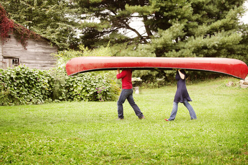 Side view of couple carrying boat on grassy field - CAVF09532